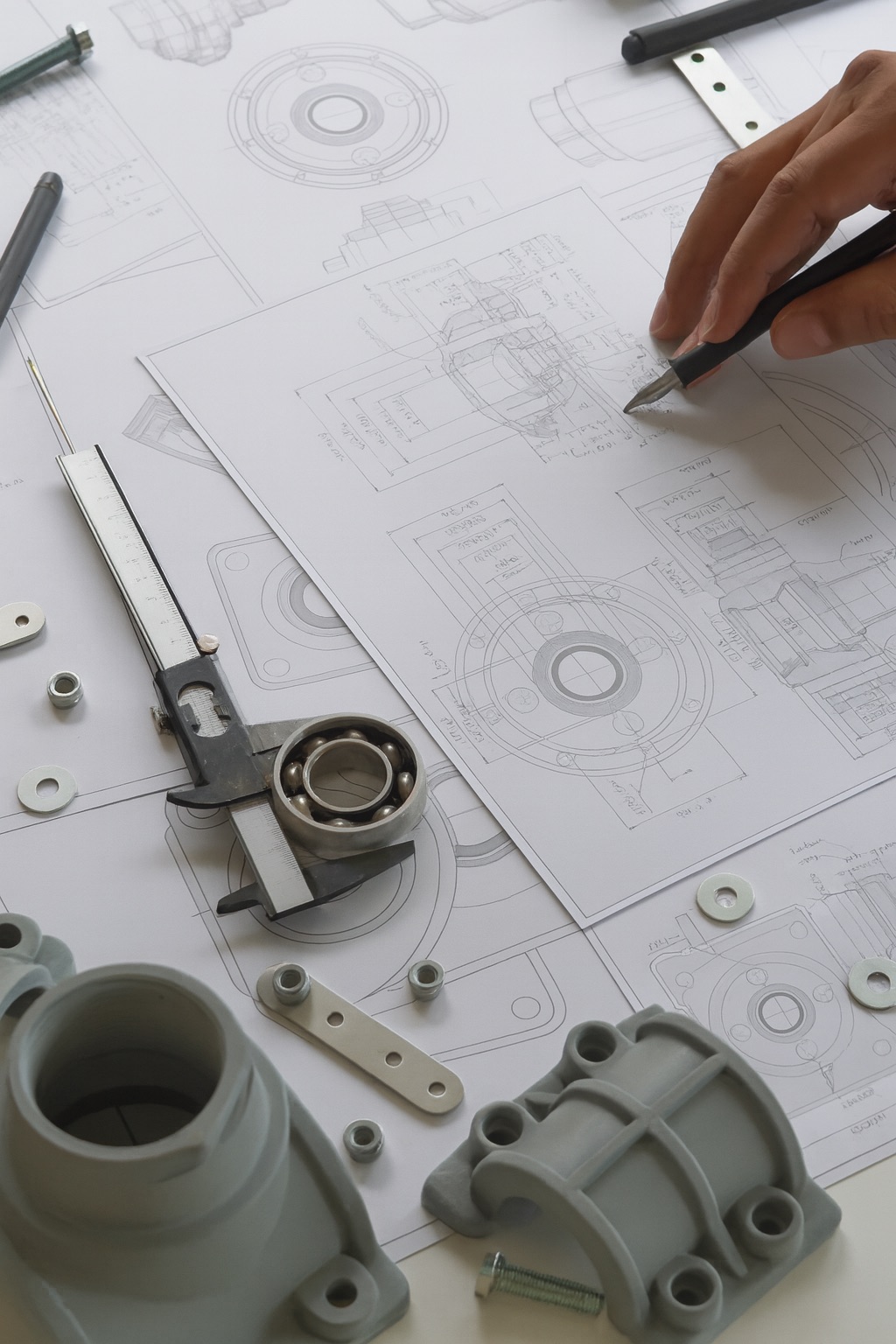 Disegni tecnici meccanici con strumenti di misura e componenti in fase di progettazione.